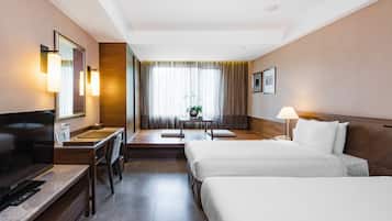 A hotel room with a TV, a desk, two beds, a lamp, and a window with curtains.