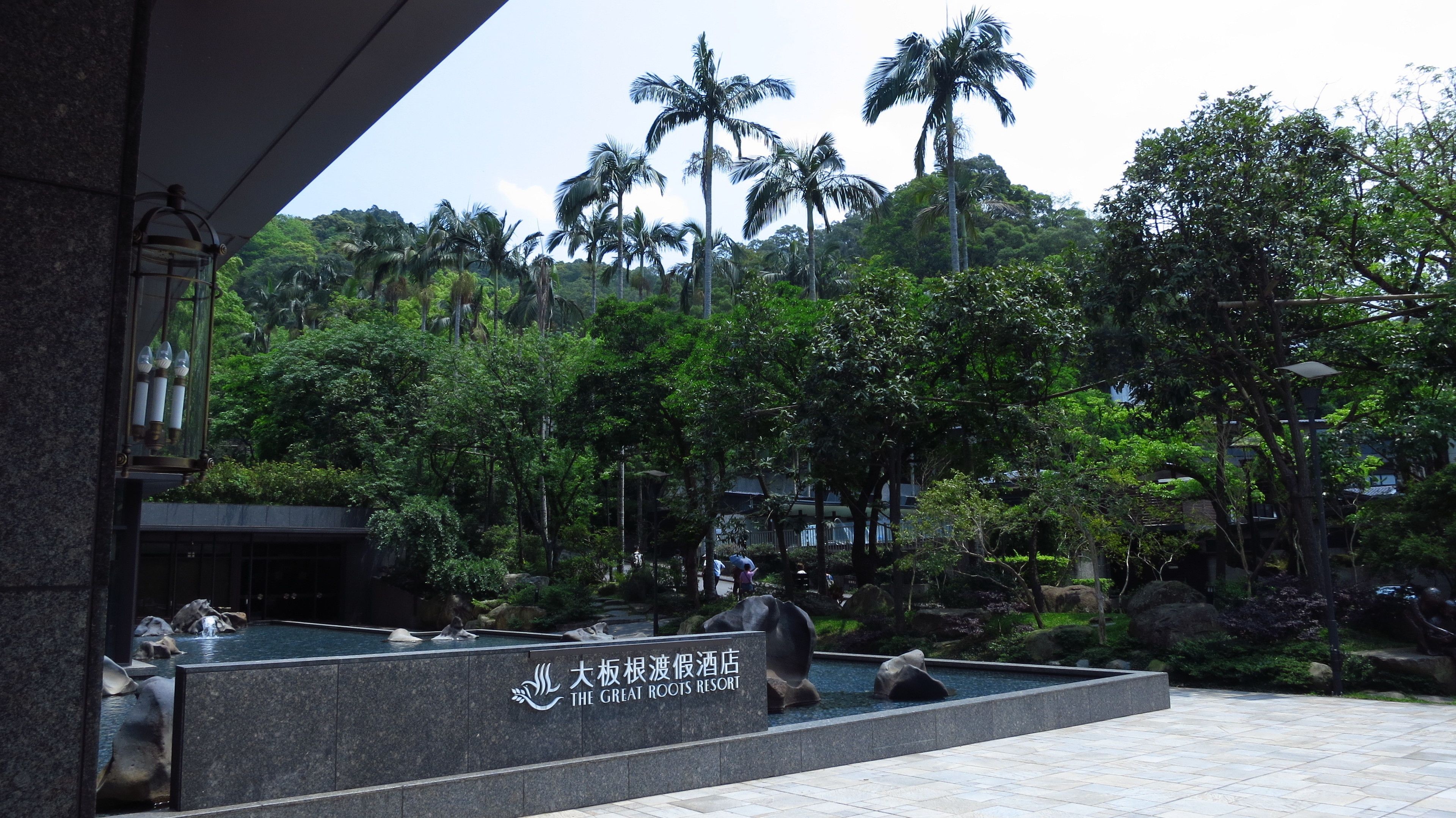 A resort with a water feature, palm trees, and a sign for 'The Great Roots Resort'.