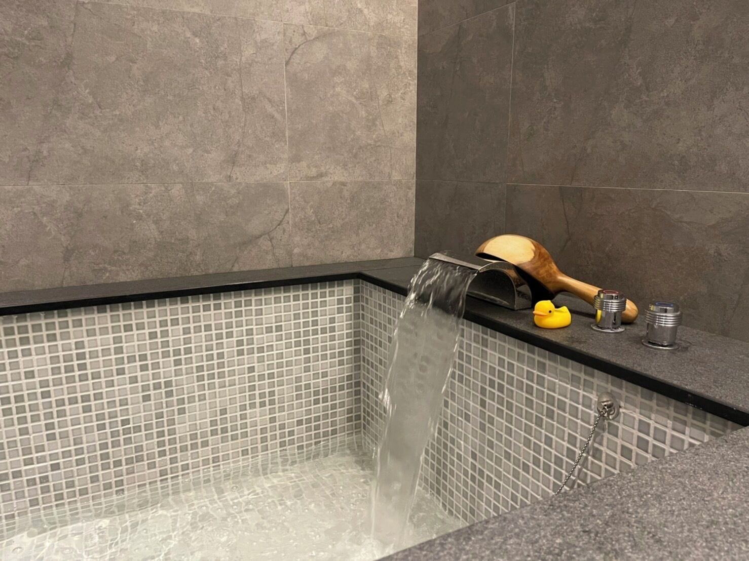 A modern bathroom with a rectangular bathtub, a wooden duck decoration, and a small yellow rubber duck.