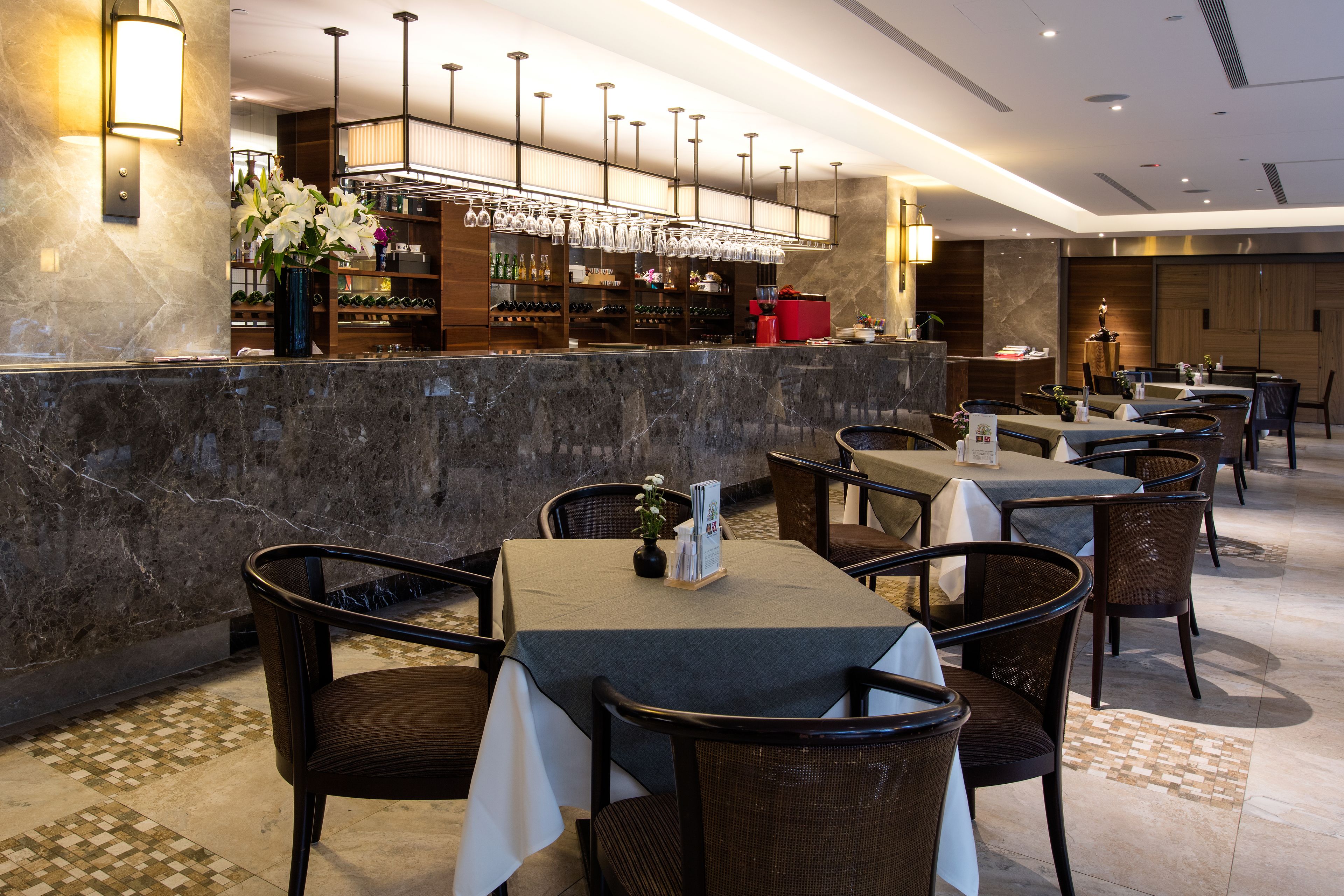 A restaurant with marble walls, a bar area with wine bottles, and multiple tables and chairs.