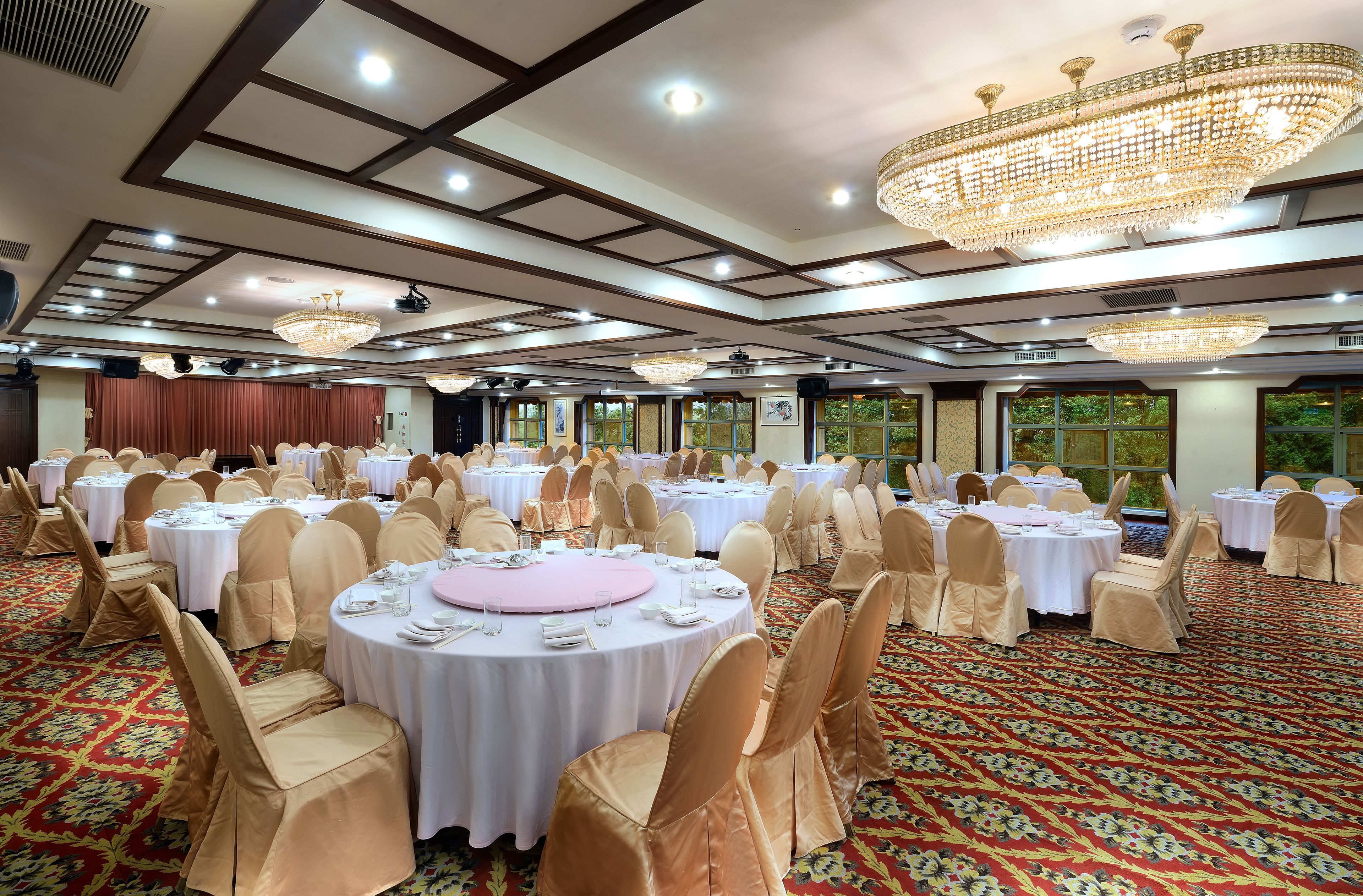 A banquet hall with round tables, chairs, and chandeliers.