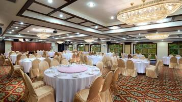 A banquet hall with round tables, chairs, and chandeliers.