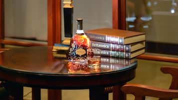 A round wooden table with a lamp, a bottle, and a stack of books.