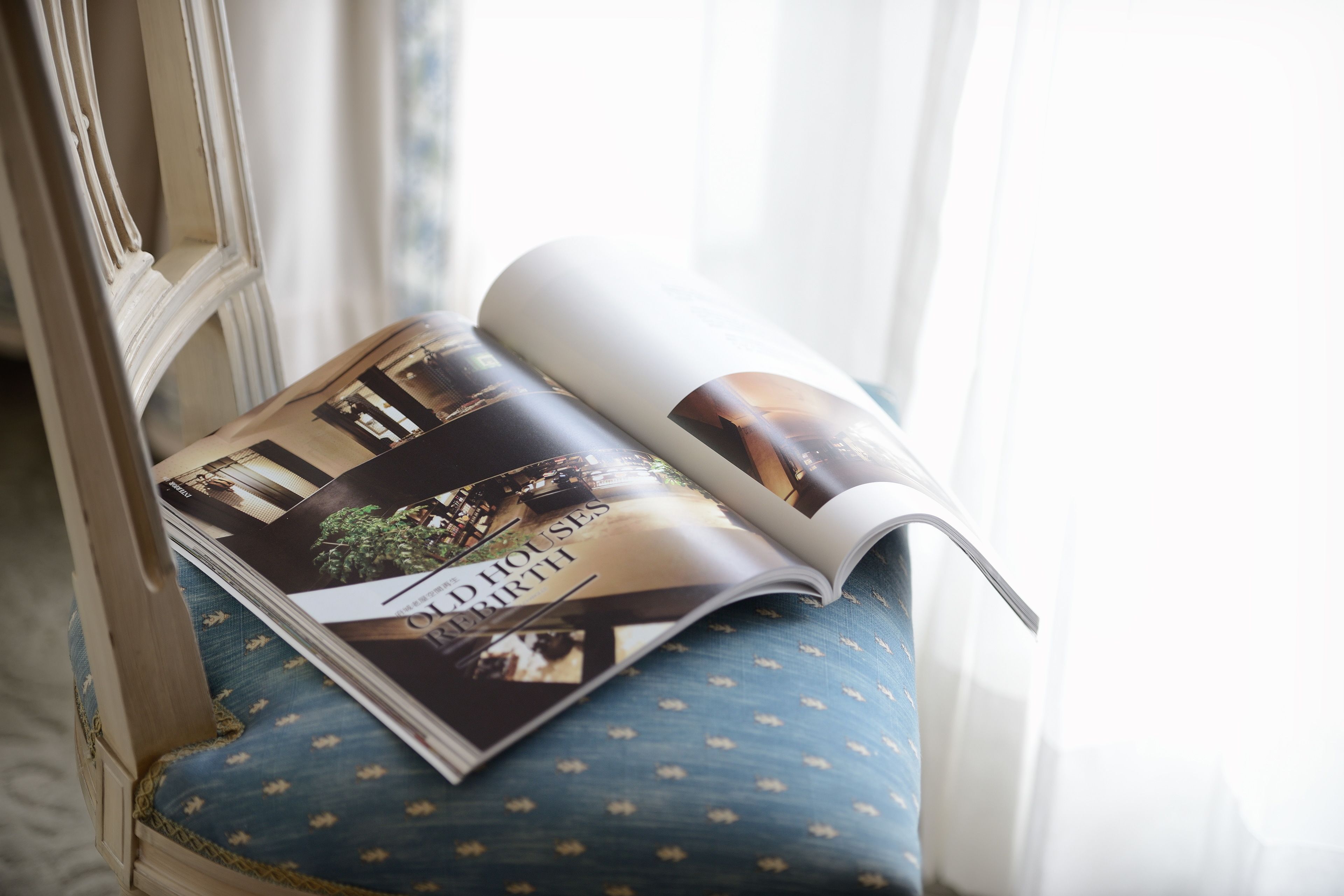Una revista abierta sobre una silla azul con lunares y estructura de madera.