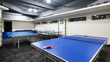 Ein Raum mit mehreren Tischtennisplatten, Teppichboden und einer Decke mit freiliegenden Balken und Leuchten.