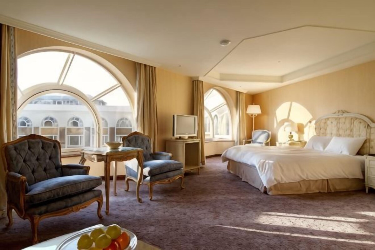 A hotel room with a large bed, a seating area with two armchairs, a small table, and a television.
