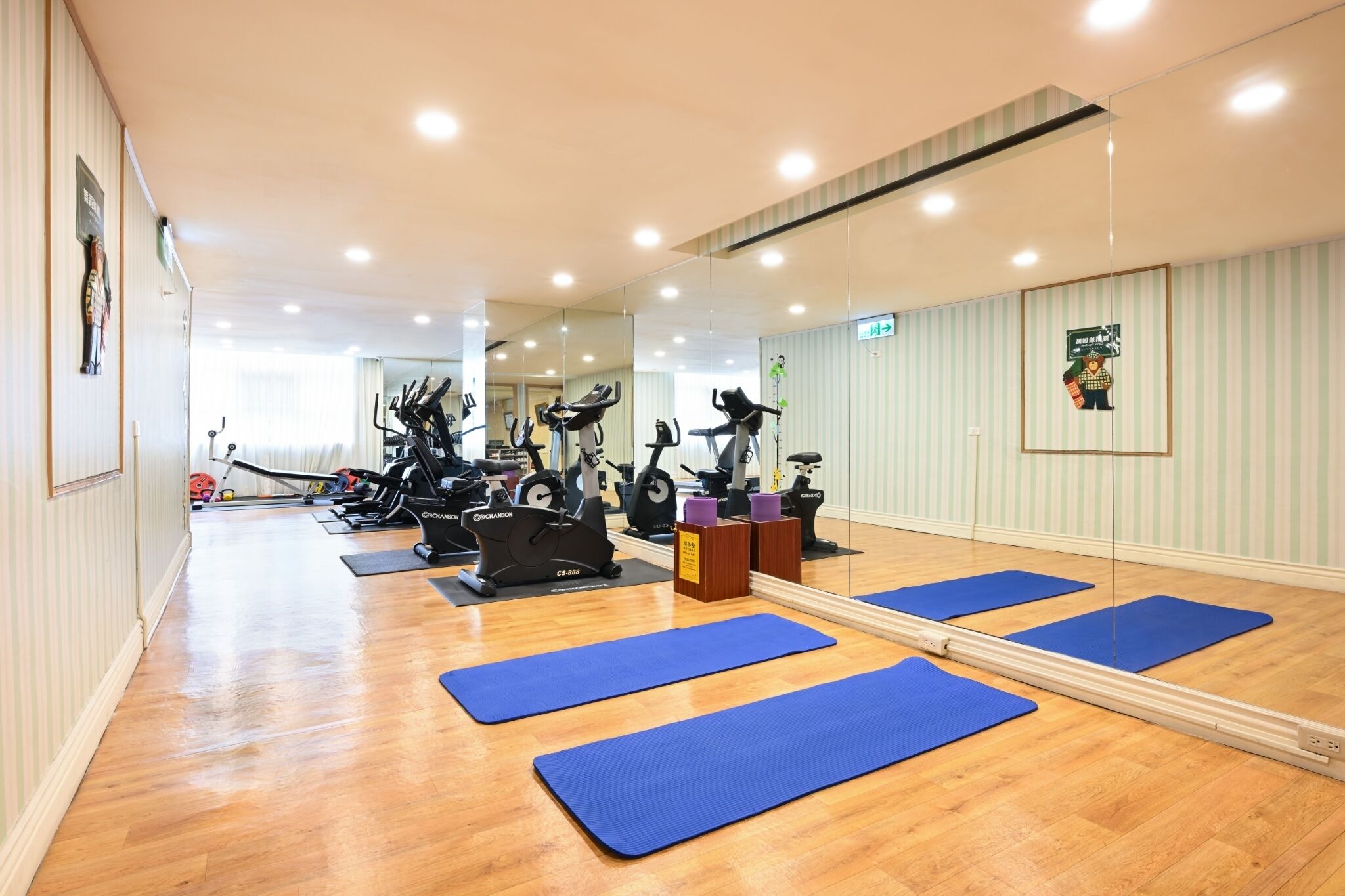 A gym with exercise equipment and blue mats on a wooden floor.
