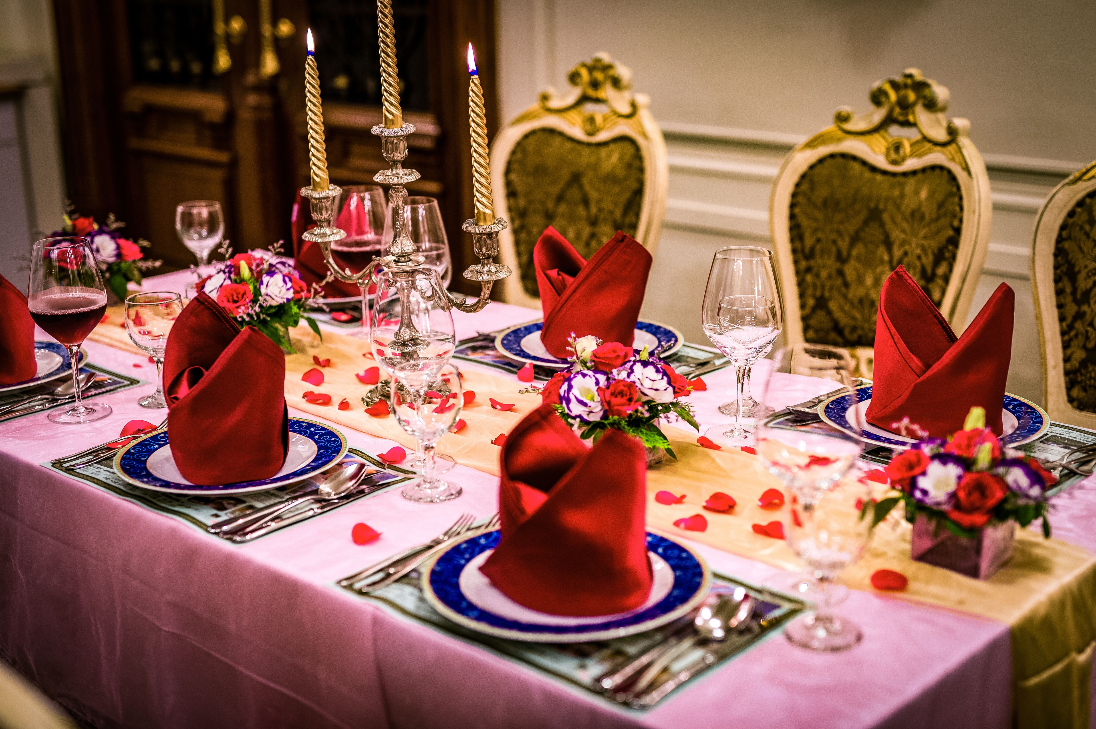 Mesa de comedor formal adornada con servilletas rojas, platos azules y blancos, y velas.