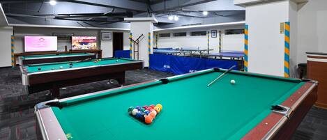 A pool hall with multiple pool tables, a billiard cue, and a television displaying a sports event.