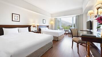 A hotel room with two beds, a desk with a television, a chair, and a view of the outdoors.