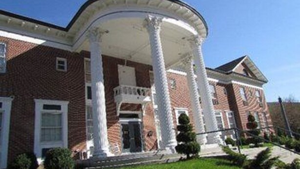 A brick building with a covered porch supported by columns, featuring a symmetrical facade and a central entrance.