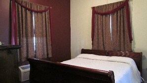 A bedroom with a wooden bed, two windows with red curtains, and a wall-mounted heater.