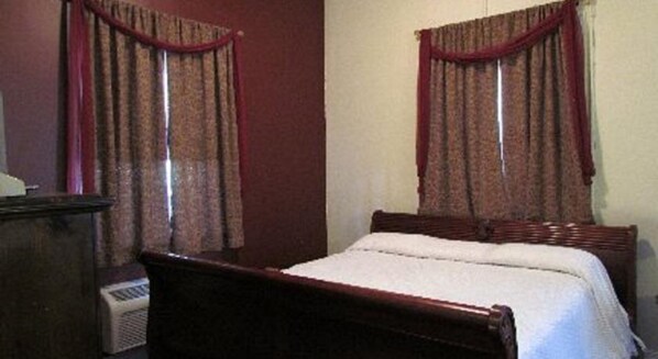 Un dormitorio con una cama de madera, dos ventanas con cortinas rojas y un calentador fijado a la pared.
