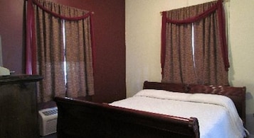 Un dormitorio con una cama de madera, dos ventanas con cortinas rojas y un calentador fijado a la pared.