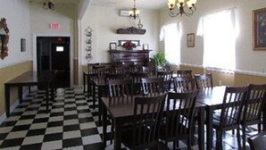 A room with a checkered floor, wooden tables and chairs, a chandelier, and a door with a red sign.