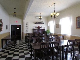 Una habitación con piso a cuadros, mesas y sillas de madera, un candelabro y una puerta con un letrero rojo.