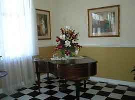 Una habitación con piso a cuadros, una mesa redonda con un jarrón de flores y dos cuadros en la pared.