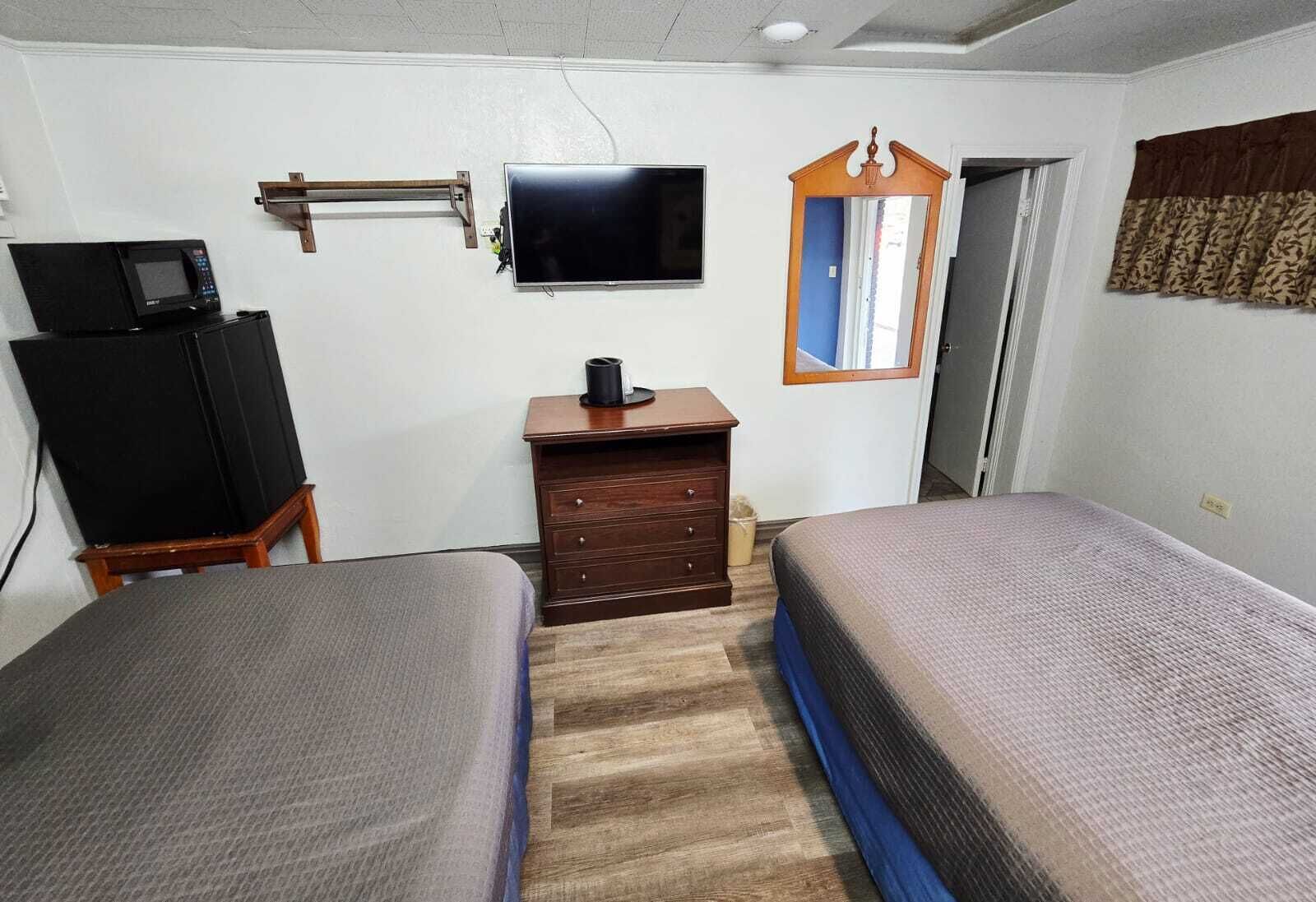 Una habitación con dos camas, televisión, cómoda y espejo.