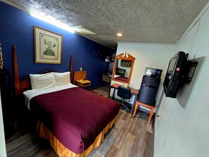 A hotel room with a bed, desk, chair, mirror, television, and a framed picture on the wall.