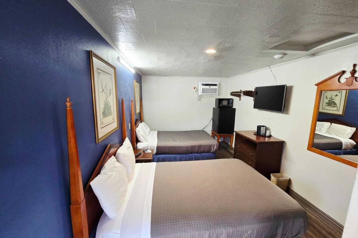 A hotel room with two beds, a TV, an air conditioning unit, and a wooden dresser.