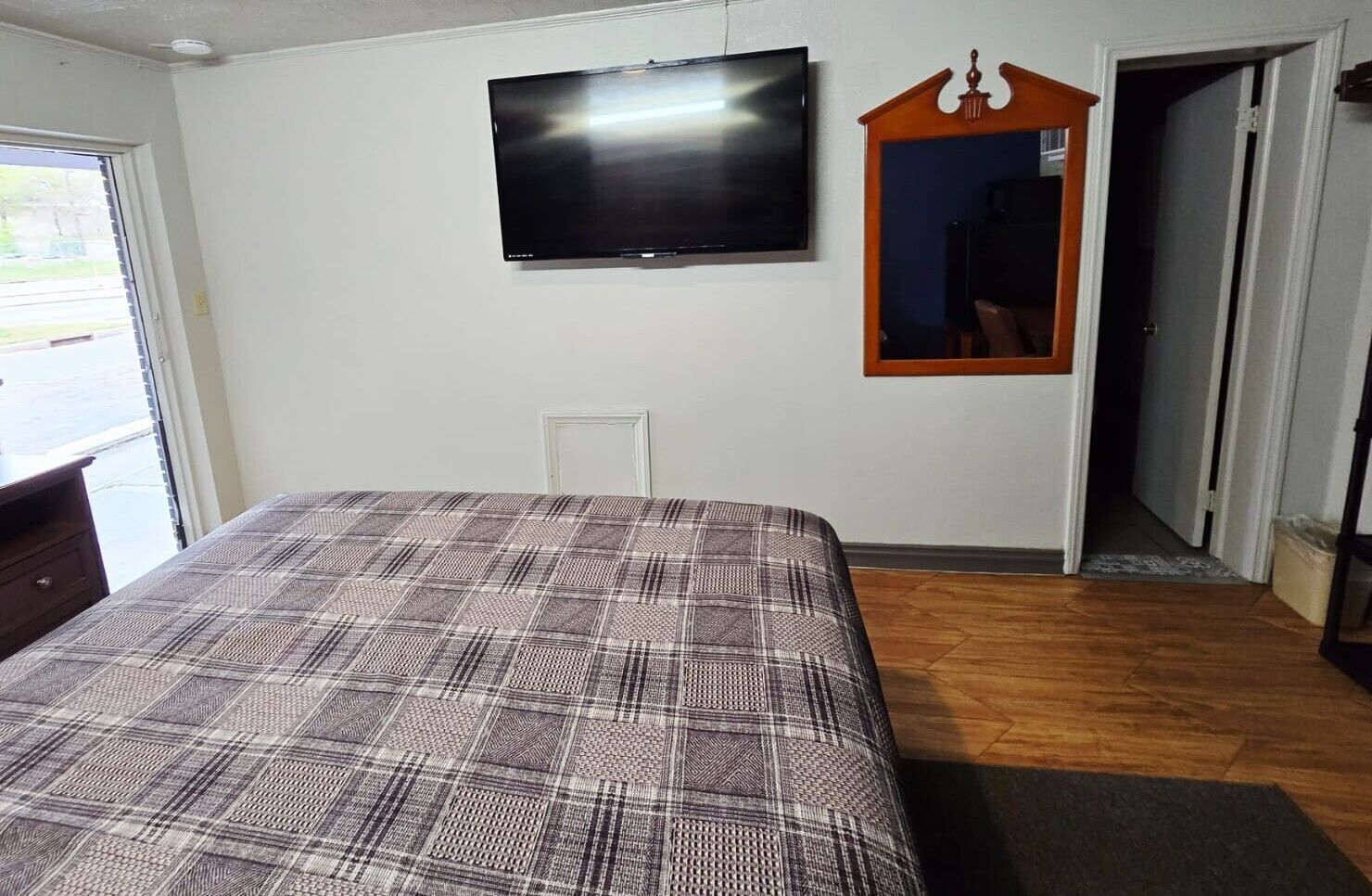 A bedroom with a bed, a television, a mirror, and a door leading to another room.