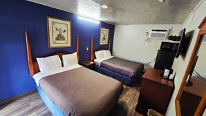 A hotel room with two beds, a desk with a computer, and framed botanical artwork on the walls.