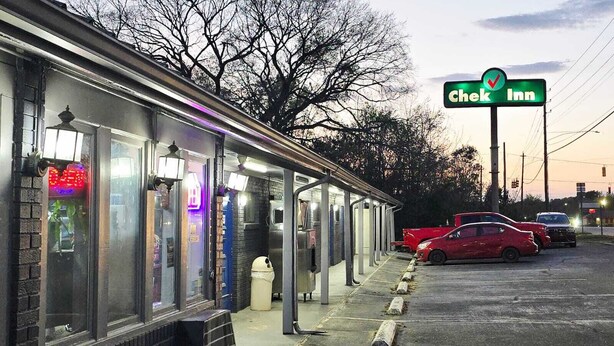 A Chek Inn with a covered outdoor seating area, a parking lot, and a clear sky.