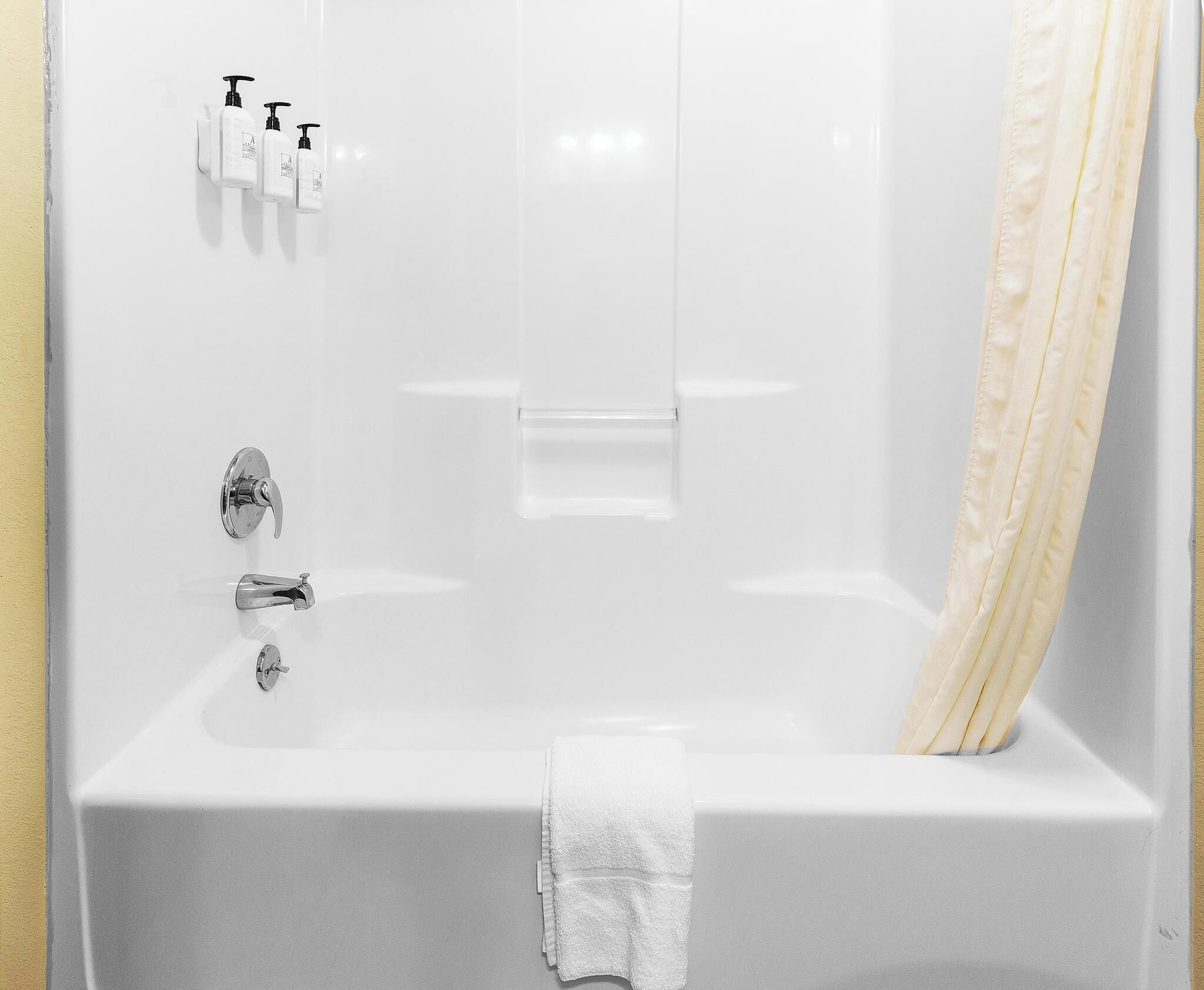 A white bathtub with a shower curtain, a towel, and two bottles of shampoo.