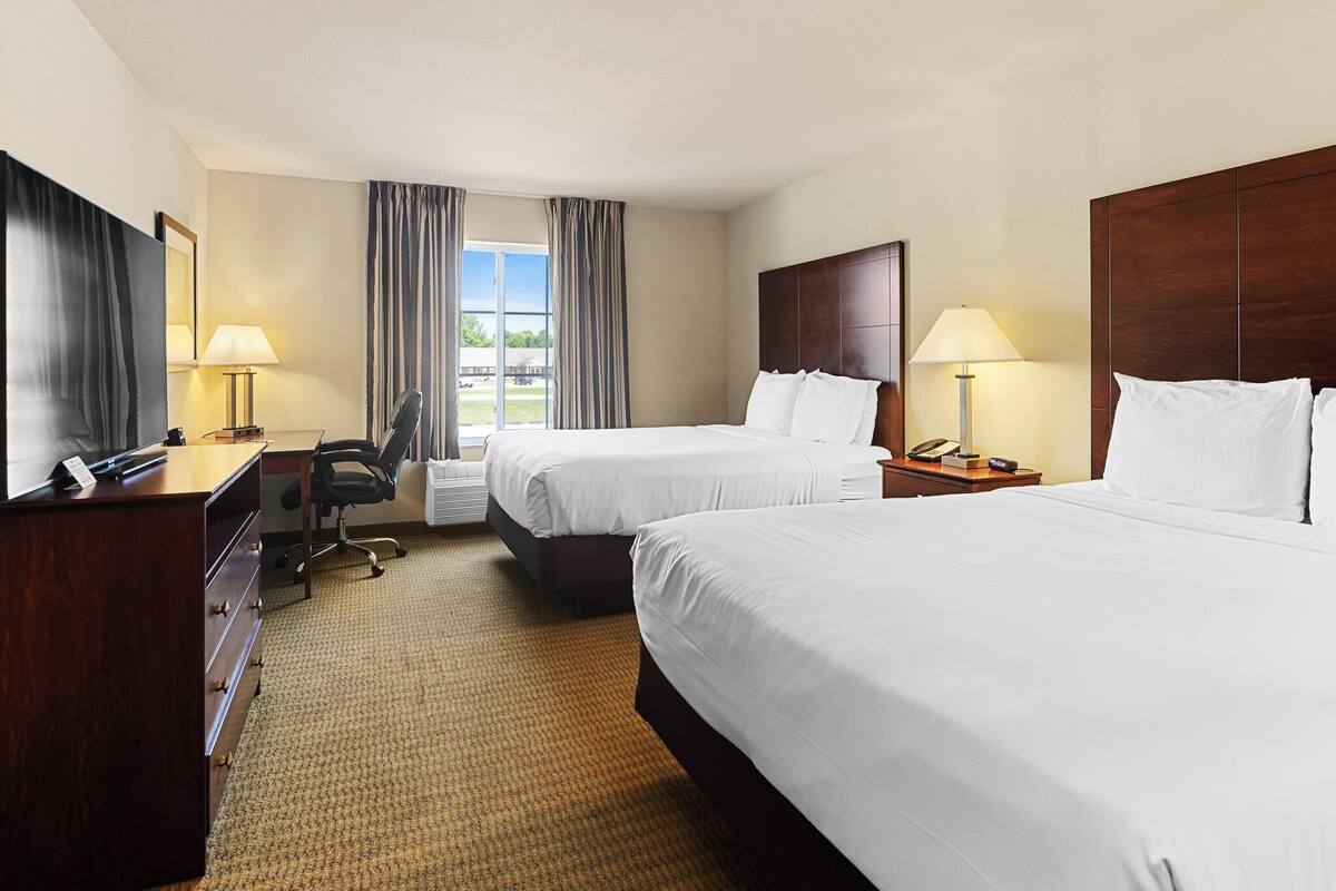 Une chambre d’hôtel avec deux lits, un bureau, une chaise et une commode.