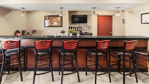 A bar area with a counter, five bar stools, a television mounted on the wall, and a door leading to another room.