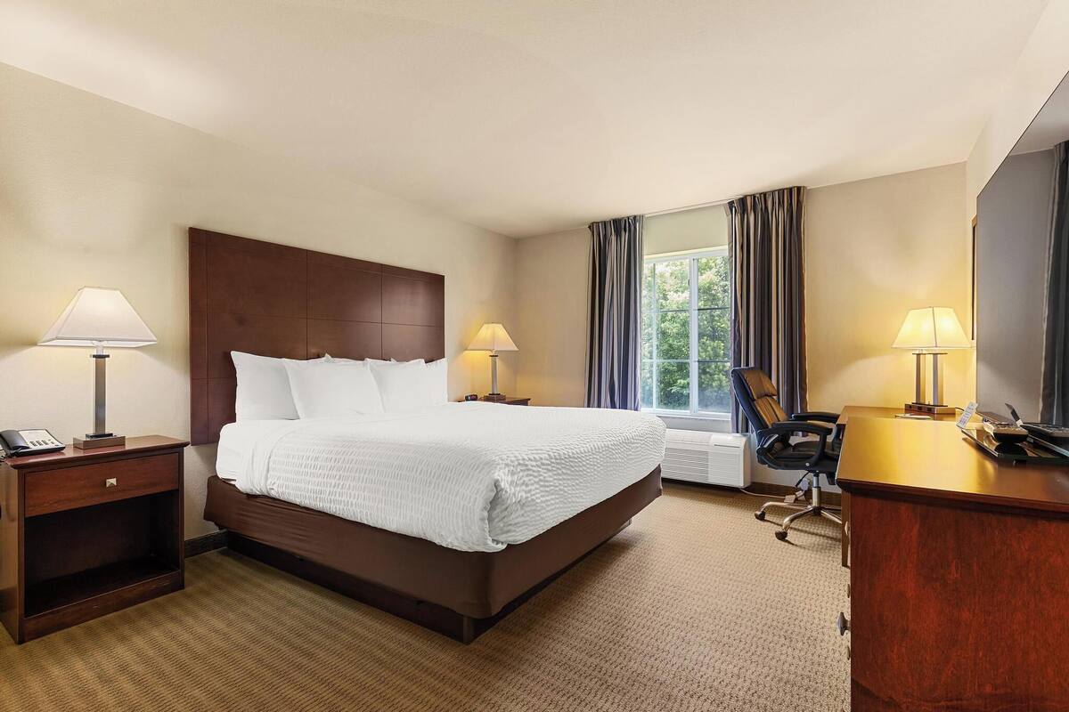 Une chambre d’hôtel avec un grand lit, deux lampes de chevet, un bureau avec une chaise et une fenêtre avec des rideaux.