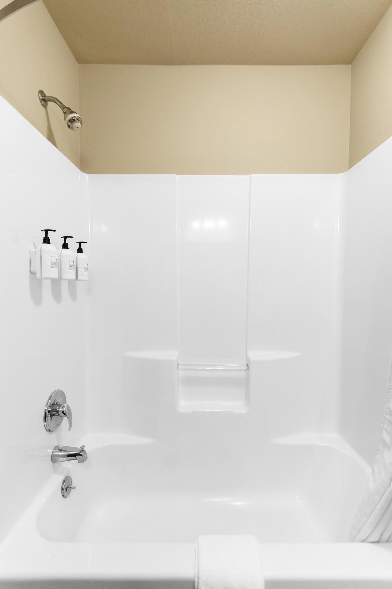 Uma casa de banho moderna com uma banheira branca, um chuveiro e três frascos de produtos de higiene na parede.