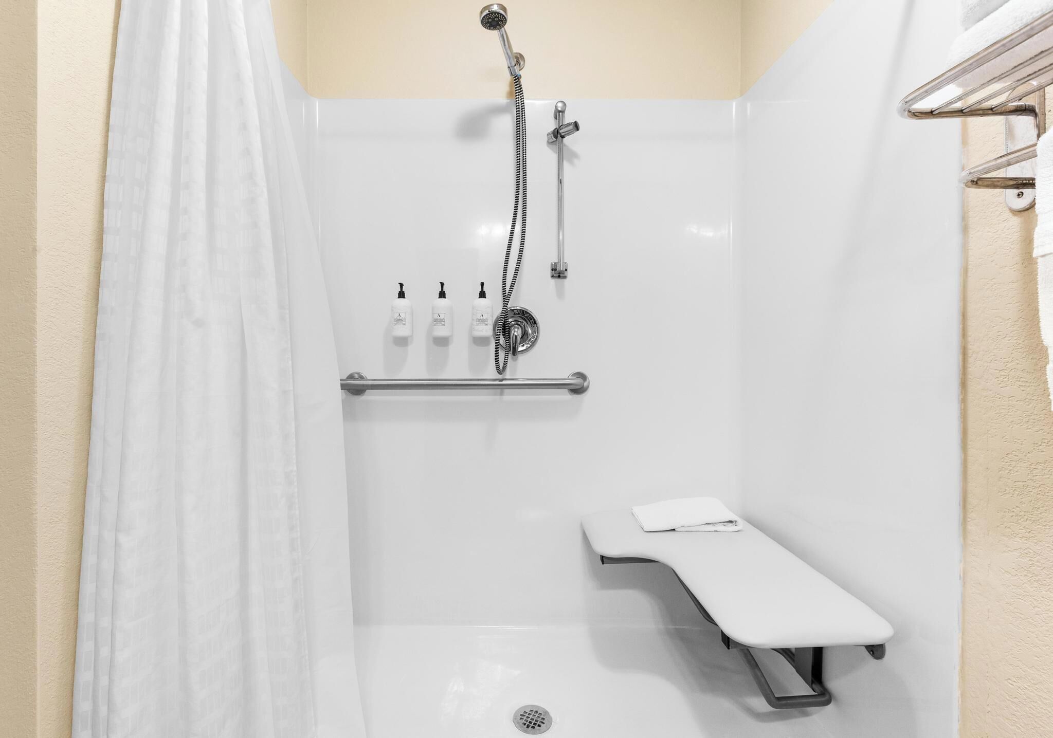Uma área de chuveiro moderna com chuveiro manual, assento embutido e porta-toalhas.