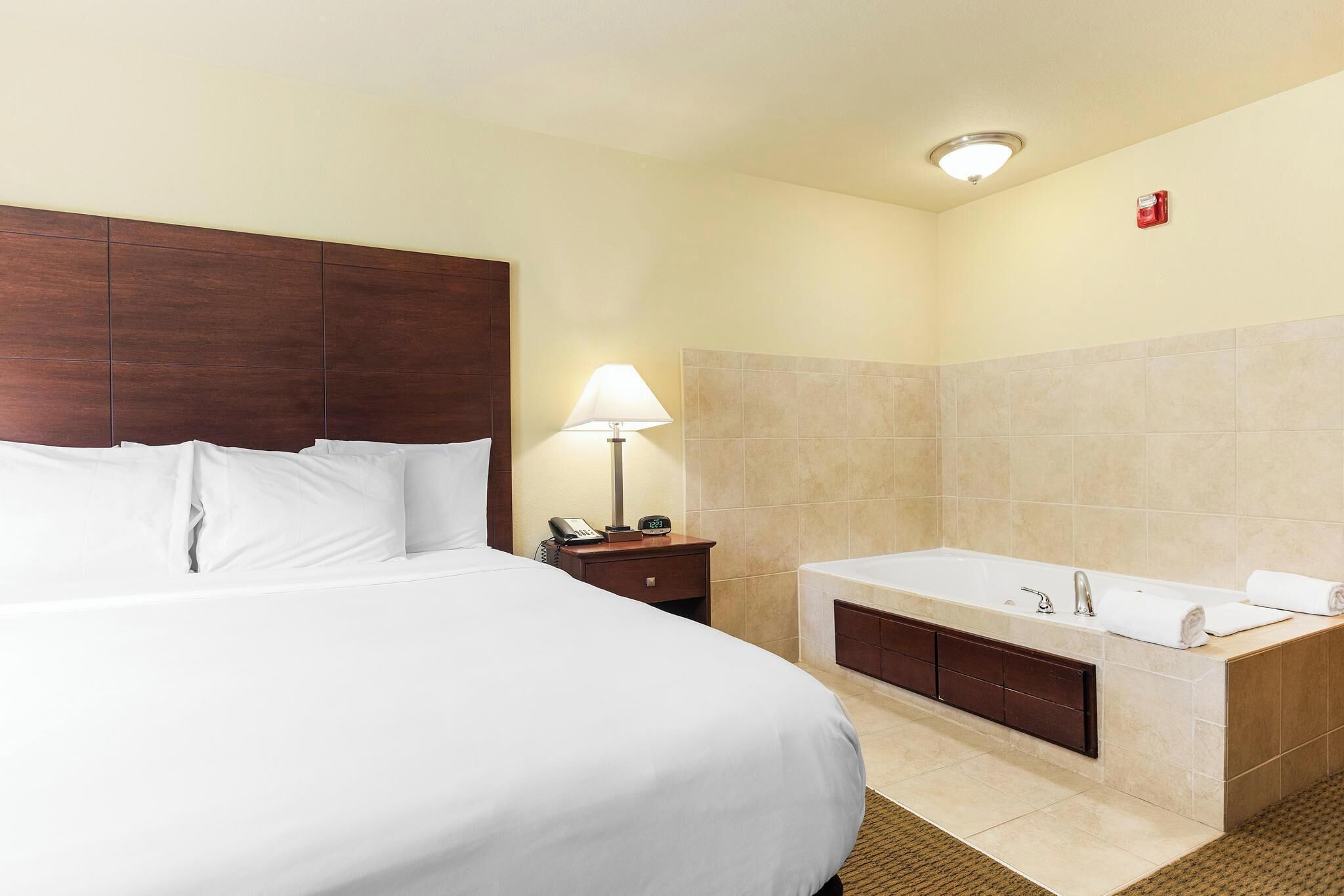A hotel room with a large bed, a bathroom with a bathtub, and a nightstand with a lamp.