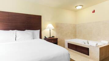A hotel room with a large bed, a bathroom with a bathtub, and a nightstand with a lamp.