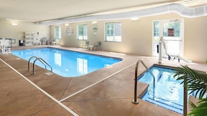 An indoor swimming pool with clear lanes, a lifeguard on duty sign, and a view of the outdoors through large windows.