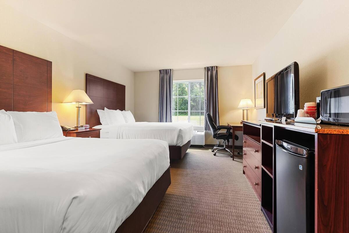 Une chambre d’hôtel avec deux lits, un bureau avec une chaise, une télévision et un mini-bar.
