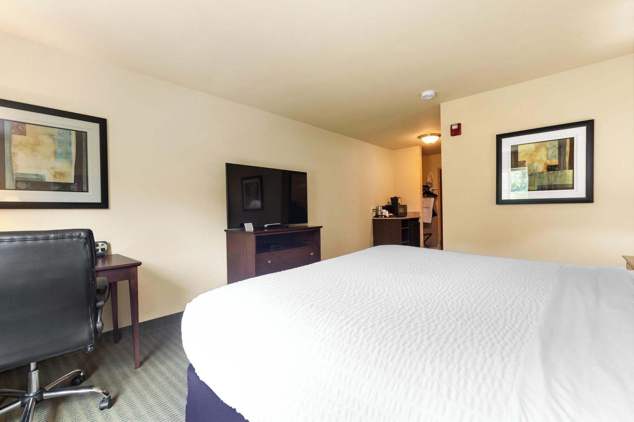 Une chambre d’hôtel avec un grand lit, un bureau avec une chaise, une télévision et des œuvres d’art encadrées accrochées aux murs.