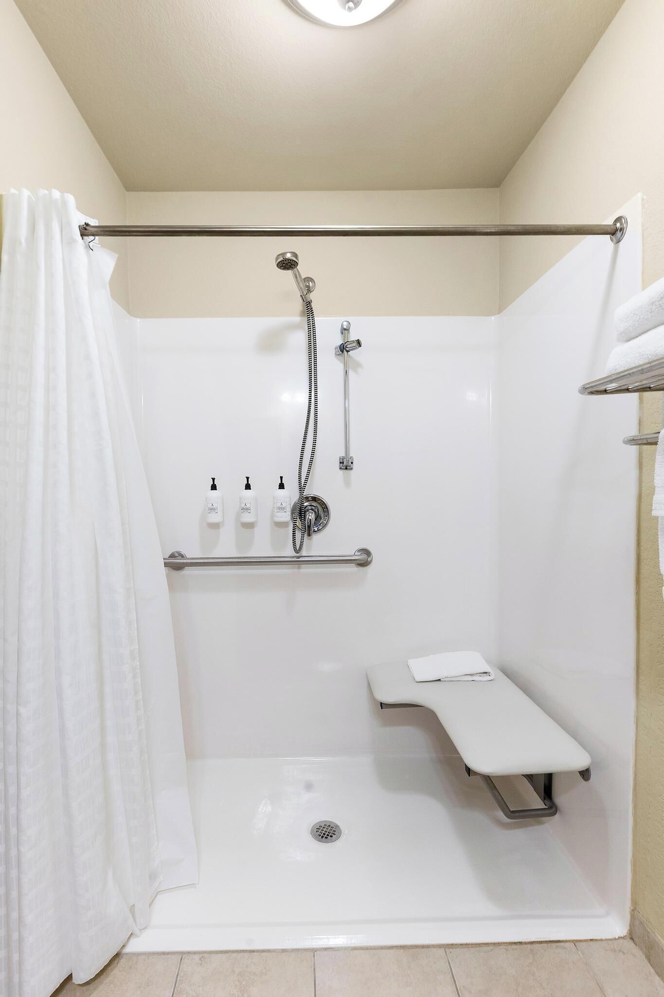 Una ducha a nivel con barra de apoyo, estante con artículos de aseo y asiento.