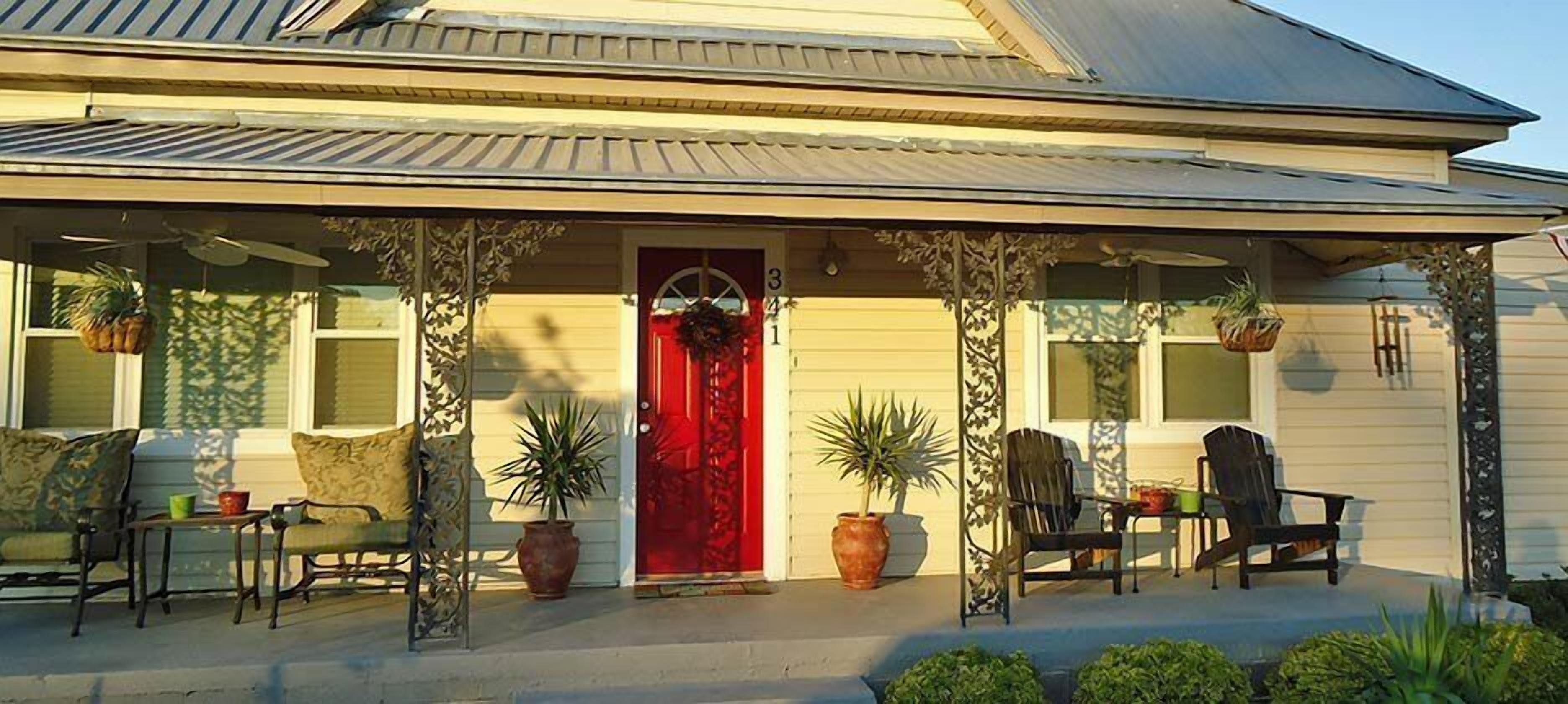 A house with a red door, a porch with chairs and potted plants, and a number '31' on the door.