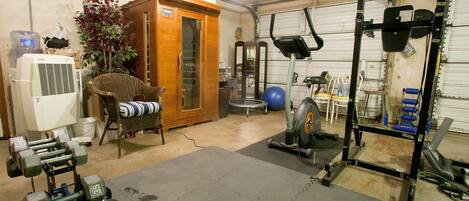 Un gimnasio en casa con equipo de ejercicio, una silla de mimbre y un armario.