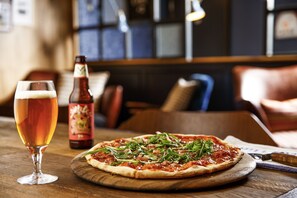 Una pizza sobre una tabla de madera, un vaso de cerveza y una botella de cerveza en una mesa de restaurante.
