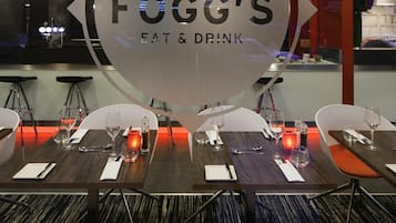Interior de restaurante con mesas dispuestas para comer, una pared de vidrio con el nombre del restaurante y una zona de bar al fondo.