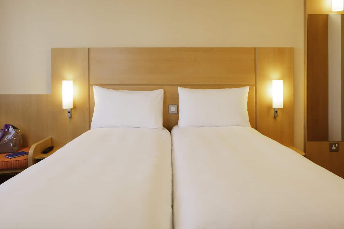 Una cama doble con dos almohadas, cabecera de madera y dos luces fijadas a la pared.