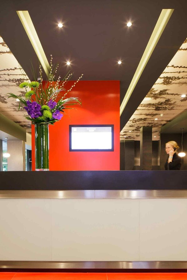 A reception area with a red wall, a large screen, and a floral arrangement.