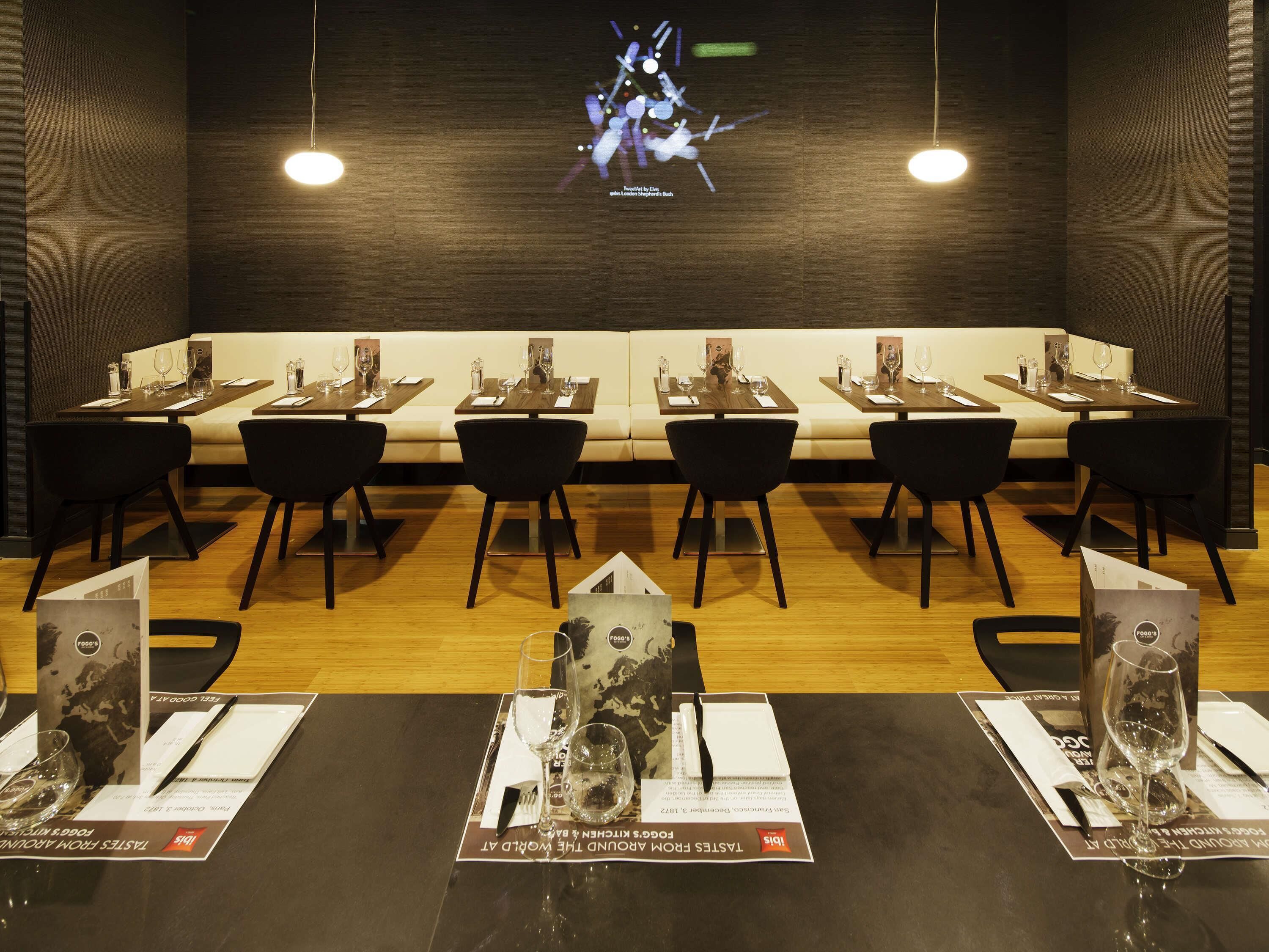 Un restaurante con mesas dispuestas para comer, una pantalla de televisión en la pared y menús sobre las mesas.