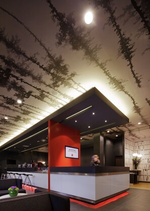 Una recepción moderna con una pared de acento roja, un letrero de bienvenida y un techo con diseños inspirados en árboles.