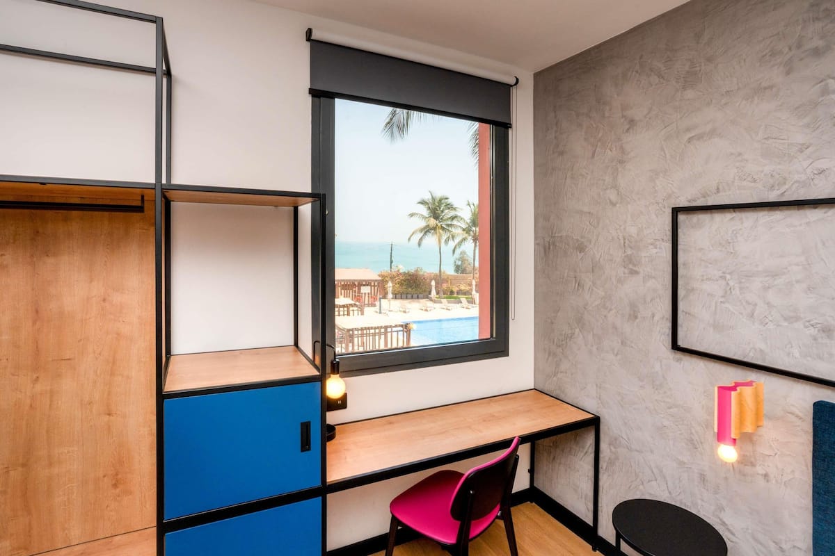 A room with a desk, a chair, and a view of an outdoor pool and palm trees.
