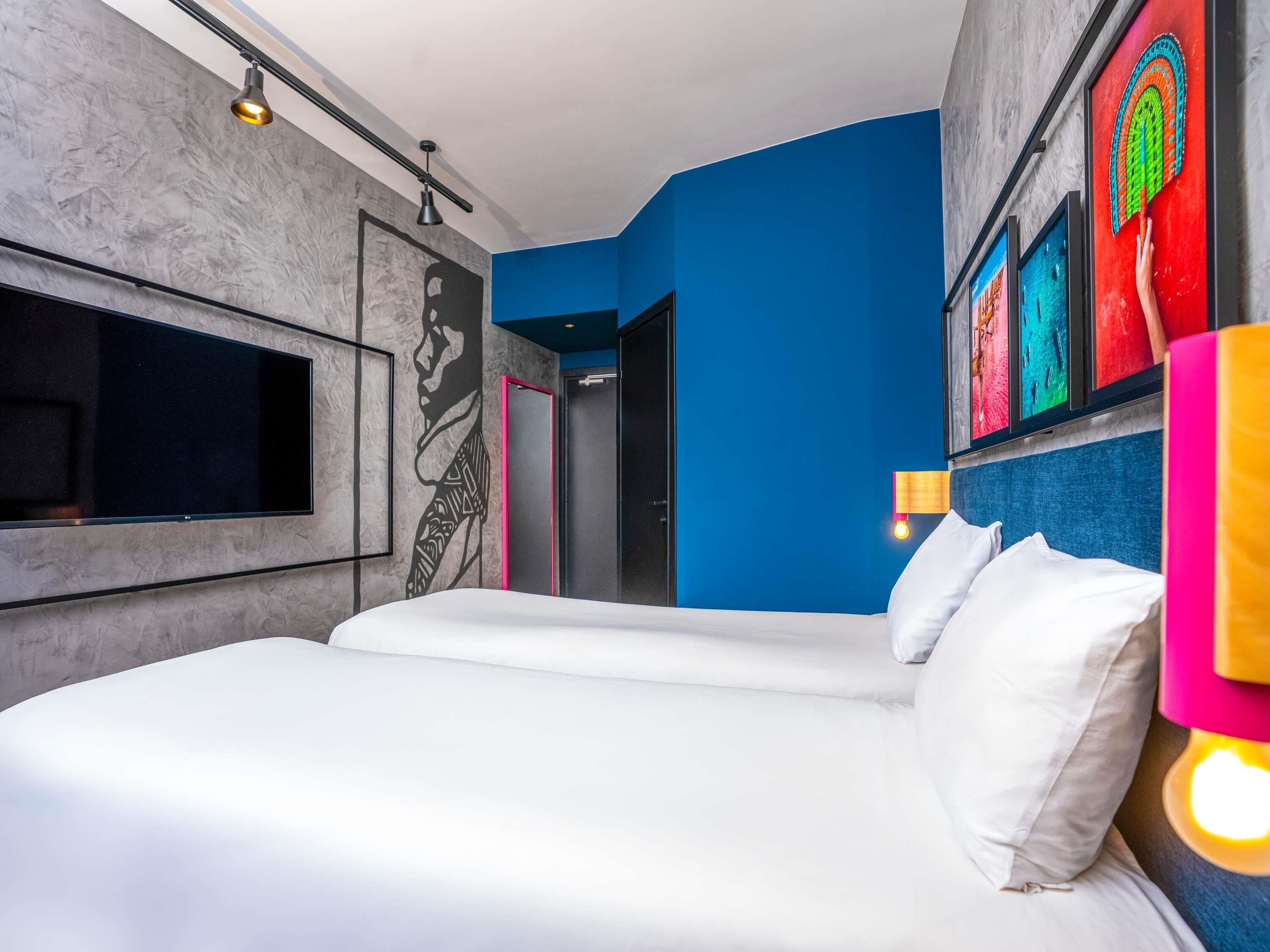 Una moderna camera d'albergo con un letto grande, una televisione a schermo piatto, un murale e opere d'arte colorate alle pareti.