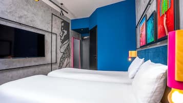 A modern hotel room with a large bed, a flat-screen TV, a mural, and colorful artwork on the wall.